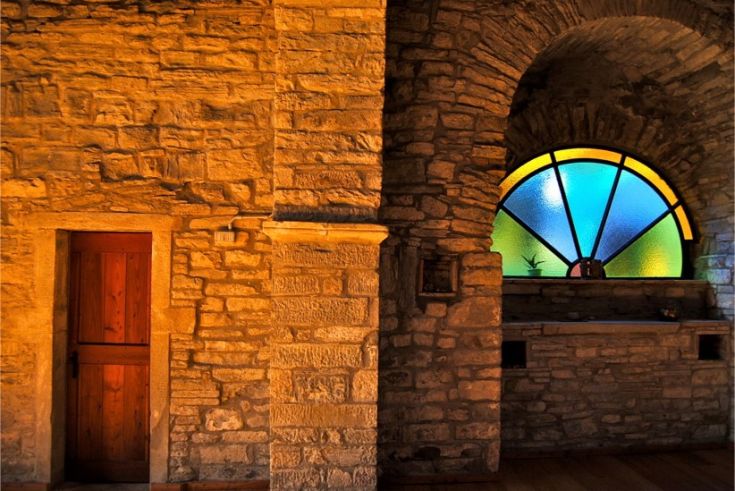 Interno di un edificio storico con pareti in pietra e una vetrata decorativa colorata.