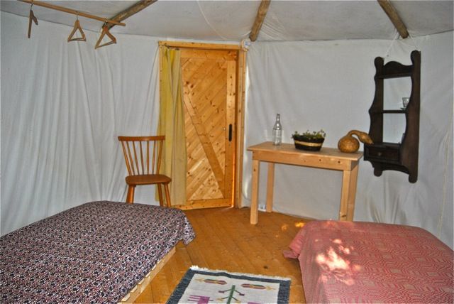 Interno di una yurta con letti, un tavolo e decorazioni sobrie, circondata dalla natura.