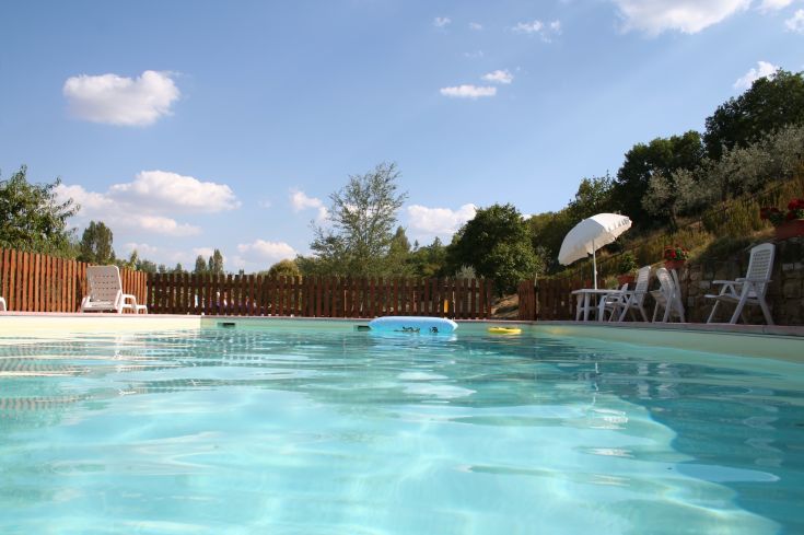 Une piscine située dans un agritourisme, entourée par la nature, avec des parasols et des transats pour se détendre.