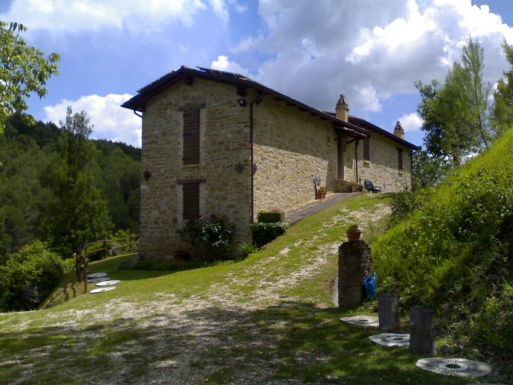 Scène d'une maison de campagne simple, entourée de verdure, d'arbres et de prairies.