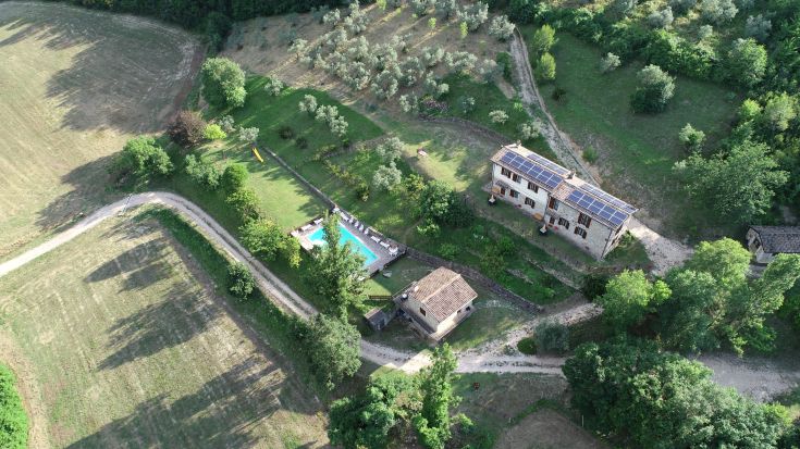 Scène d'un agriturismo situé sur une colline, entouré de verdure et doté d'une piscine extérieure.
