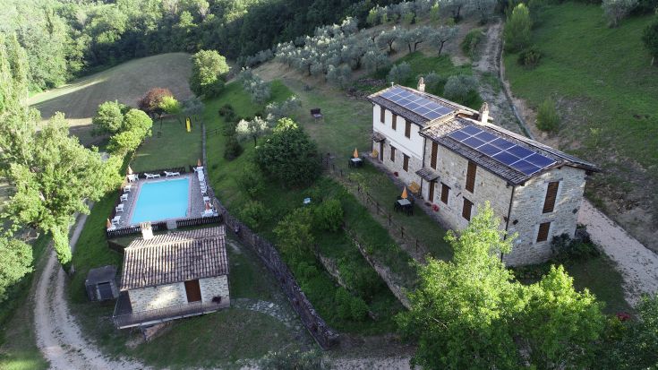 Scène d'une ferme rurale située sur une colline, entourée de verdure, avec une piscine et des appartements de style rustique.