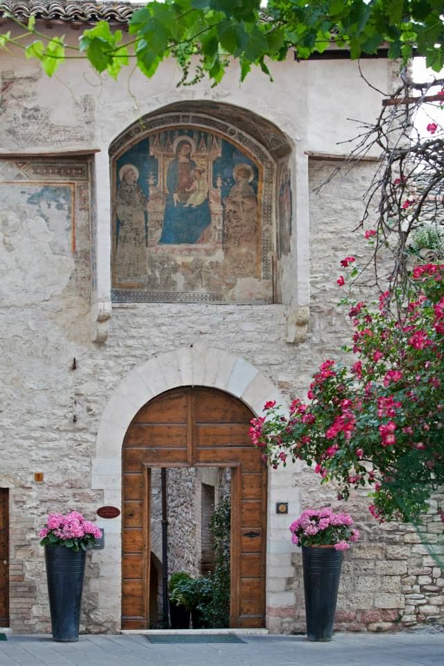 Portone d'ingresso decorato con piante, situato davanti a un palazzo di Assisi.