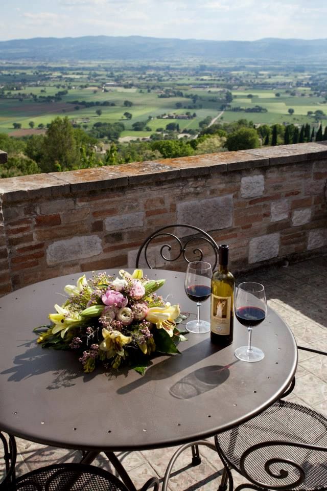 Un tavolo semplice con del vino rosso e fiori, con vista su un'area verde.