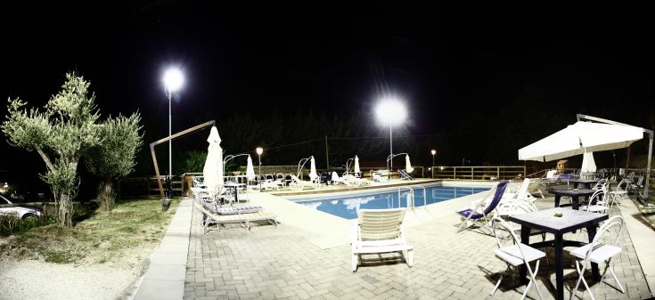 Un'area di tranquillità caratterizzata da una piscina illuminata, circondata da vegetazione e ombrelloni.