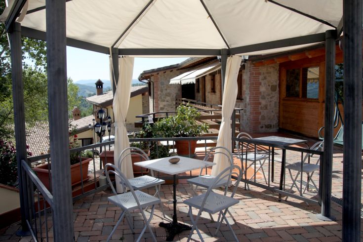 Sotto un gazebo, un tavolo e delle sedie offrono una vista su un tranquillo panorama. Ambiente semplice e rilassante.