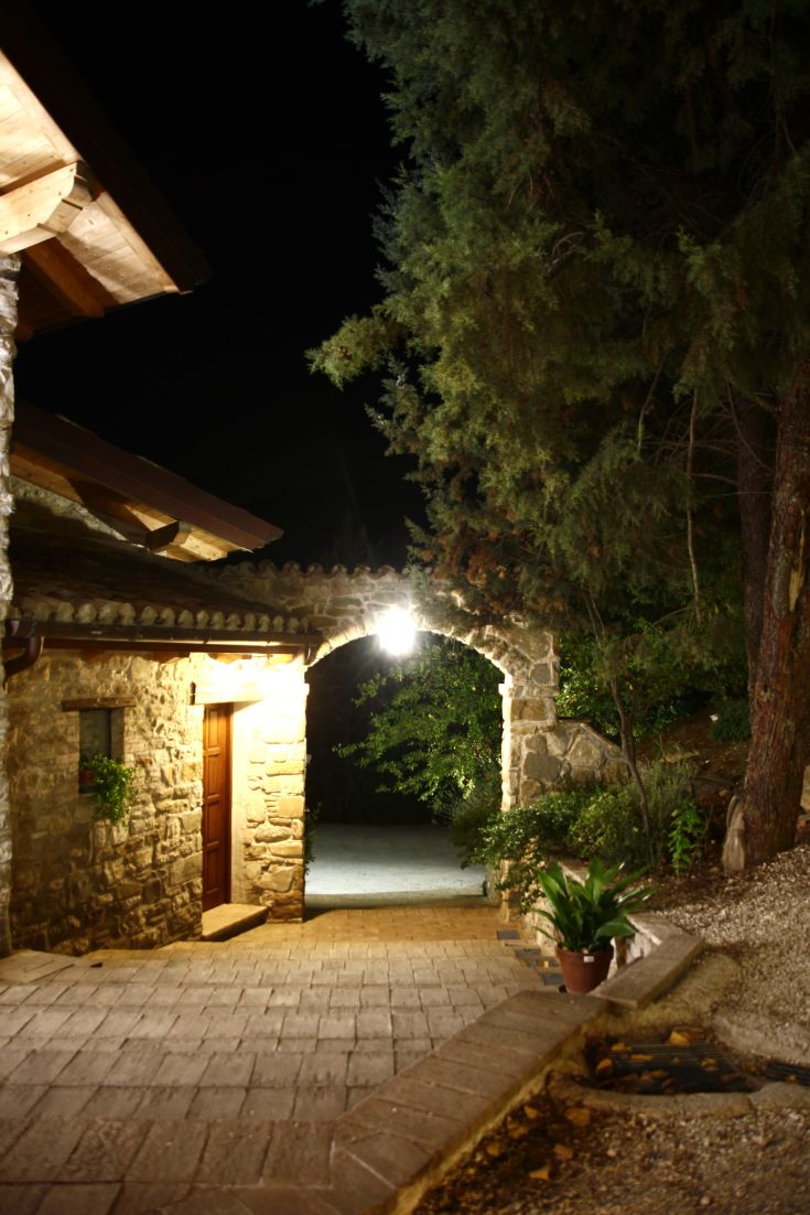Inquadratura notturna di un tranquillo albergo circondato da vegetazione, con luci calde che lo illuminano.