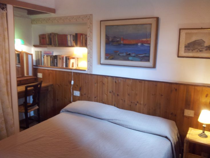 Camera semplice con letto, libreria e tavolo. Atmosfera tranquilla e accogliente.