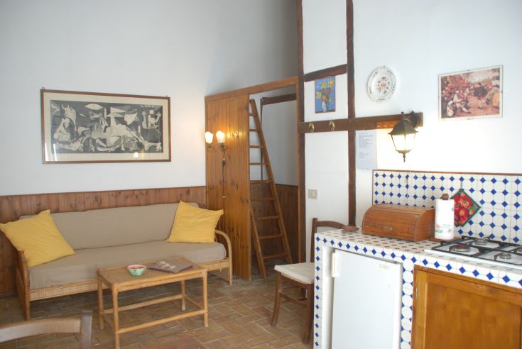 Interno di un appartamento con soggiorno, cucina e scala a scomparsa, decorato in modo semplice e rustico.