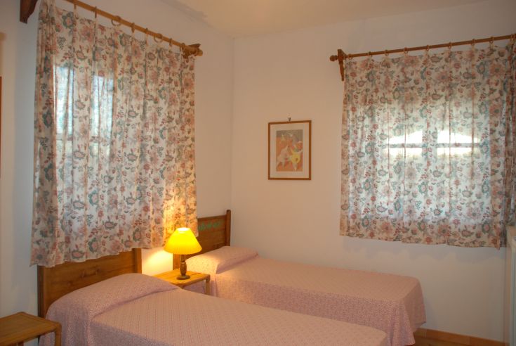 Ambiente confortevole con letti singoli e tende a motivi floreali, ideale per un soggiorno tranquillo.