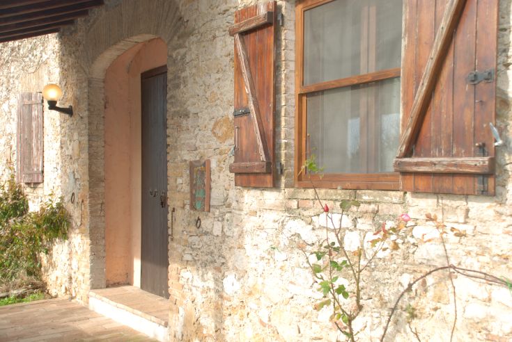 Struttura rurale con porte e finestre in legno, circondata da muri di pietra.