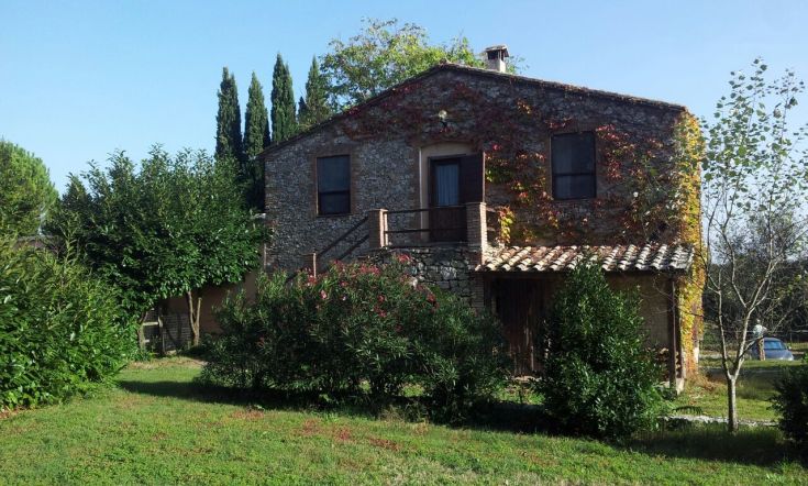 Un edificio in pietra immerso in un giardino ordinato, circondato da vegetazione naturale.