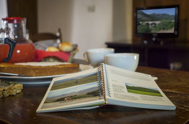 Una colazione composta da dolci e bevande, con un libro aperto e la televisione accesa, creando un'atmosfera di relax.