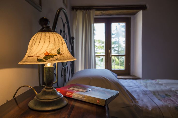 Una lampada illumina una stanza con panorama sulla natura. Un libro è riposto sul comodino.