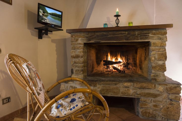 Camino tradizionale e poltrona nel soggiorno, ambiente semplice e rilassato.