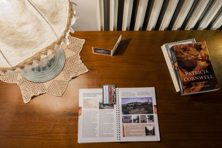 Tavolo con diverse libri, una lampada accesa e una guida di viaggio aperta su Spello.