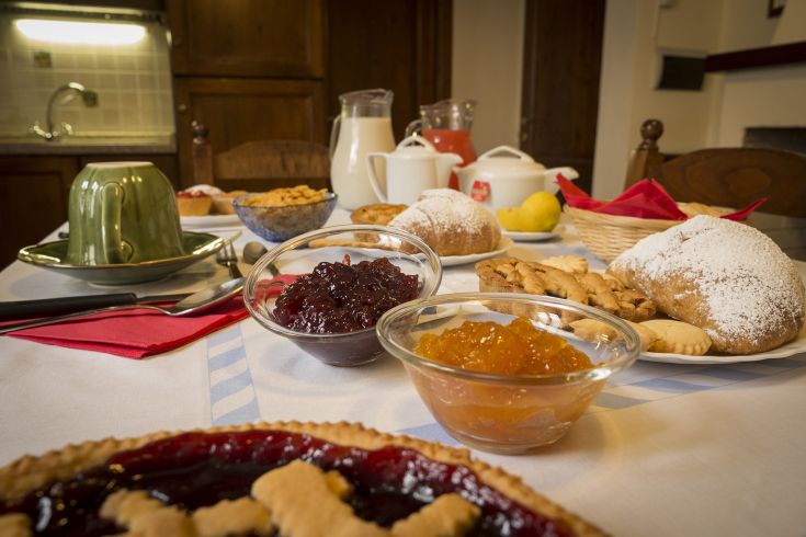 Colazione abbondante con dolci, marmellate e diverse bevande calde e fredde servita in un ambiente accogliente.