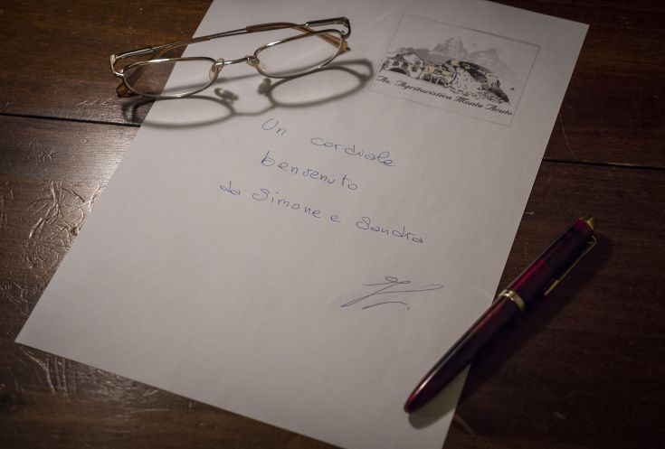 Una lettera di benvenuto poggiata su un tavolo di legno, accanto a un paio di occhiali e a una penna rossa.