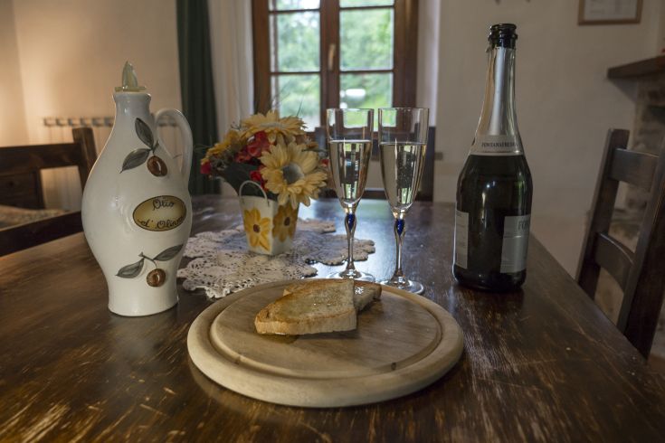 Un tavolo imbandito con olio d'oliva, pane, fiori e spumante, creando un'atmosfera accogliente.