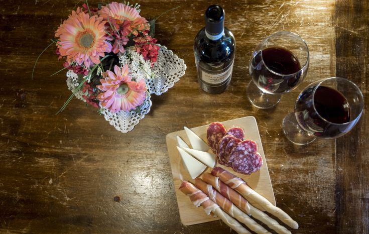Tavola apparecchiata con vino rosso, salumi, formaggi e fiori, ideale per stare insieme con amici.