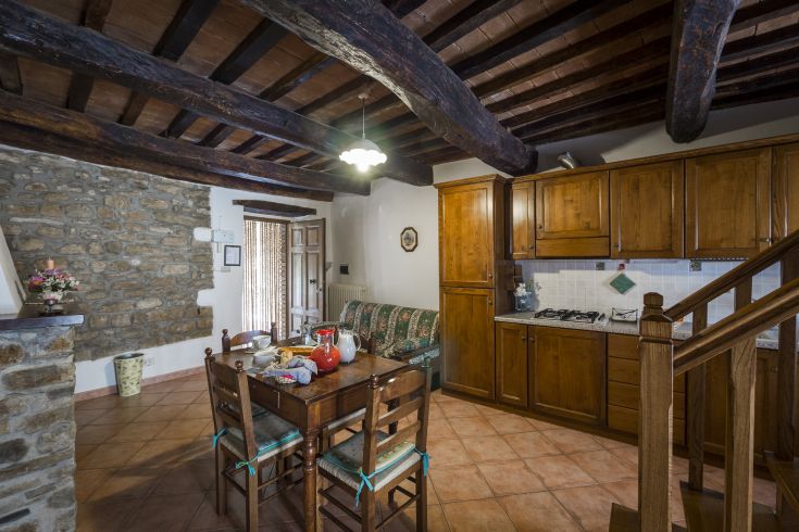Cucina calda e familiare con travi in legno, arredamento semplice e zona soggiorno. Spazio adatto per il relax.