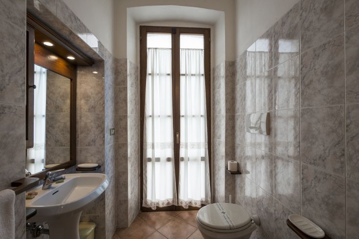 Bagno sobrio con tonalità chiare, arricchito da dettagli in marmo e luce naturale proveniente dalle finestre.