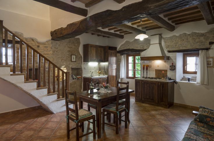 Soggiorno semplice con cucina e tavolo in legno, atmosfera calda e accogliente.