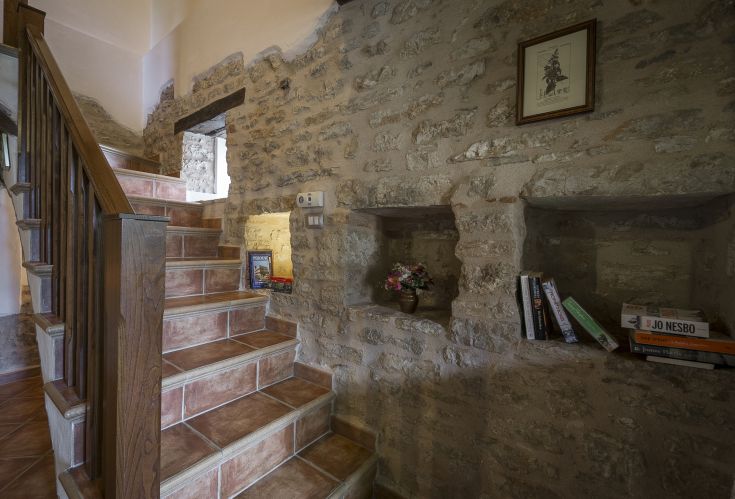 Ambiente con scale in legno e pareti in pietra, arredato con libri e decorazioni semplici.