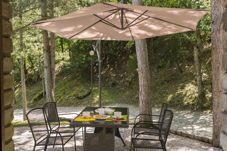 Un tavolo all'aperto con un grande ombrello, circondato da alberi e vegetazione, ideale per un momento di relax.