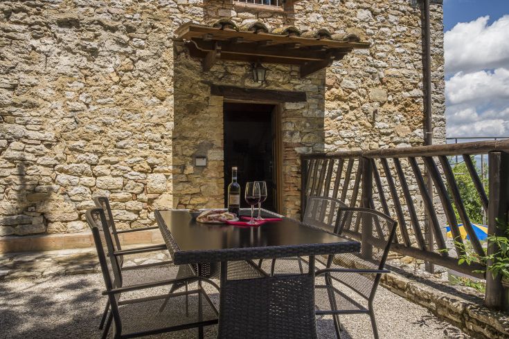 Un tavolo all'aperto in prossimità di un edificio in pietra, con bottiglie di vino e bicchieri disposti per un momento di relax.