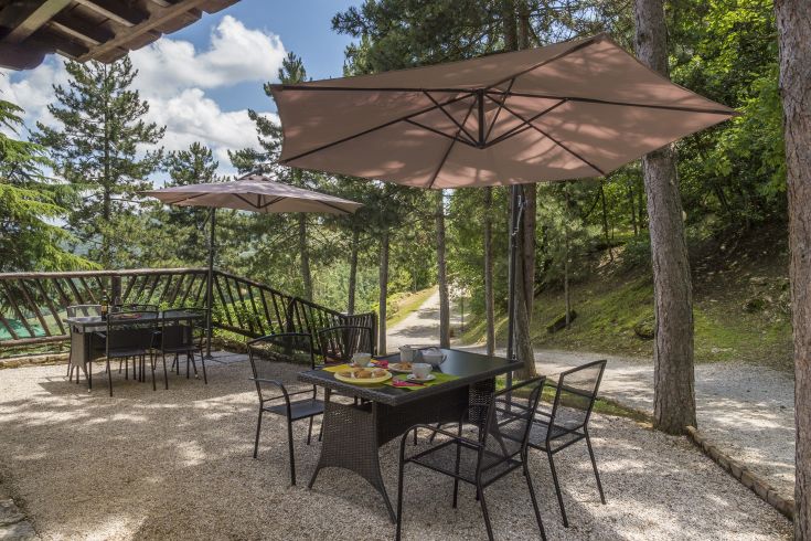 Un'area all'aperto tranquilla, circondata da vegetazione, con tavoli e ombrelloni per ripararsi dal sole.