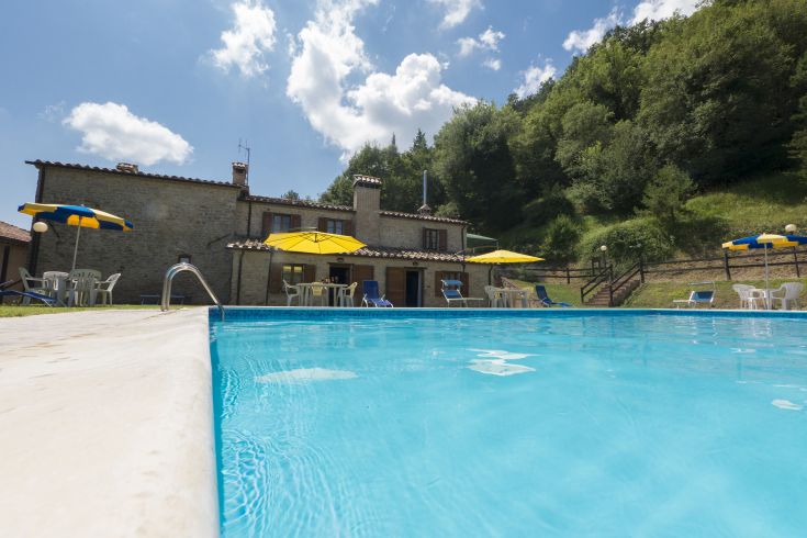 Un agriturismo immerso nella natura, dotato di una piscina e di ombrelloni gialli per momenti di relax.