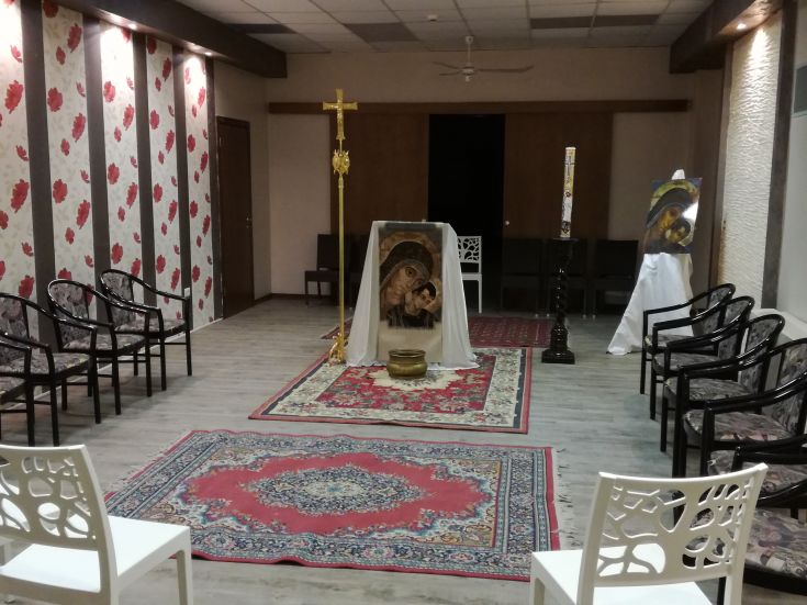 An indoor prayer area with chairs arranged around a carpet, a small altar, and some sacred images.