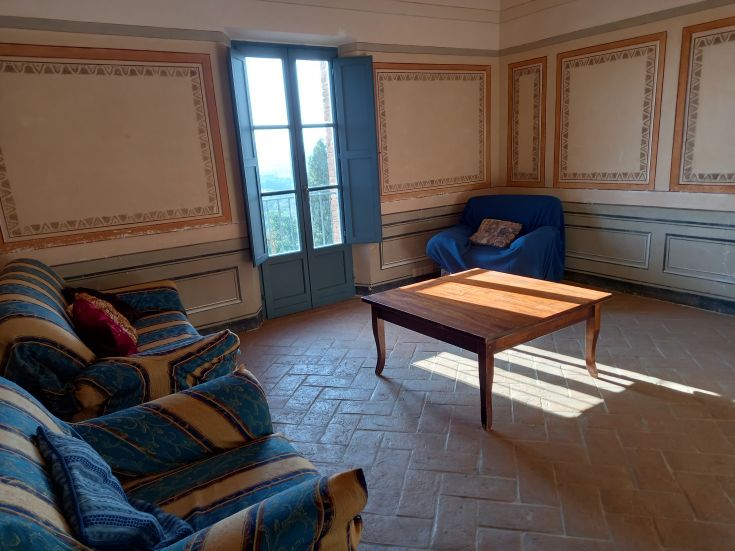 Interno di una stanza confortevole con divani e un tavolo, illuminata da luce naturale che entra da una finestra.