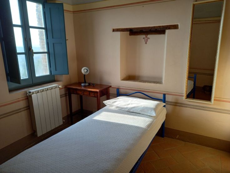 Stanza semplice con letto singolo, finestra di colore blu e arredo sobrio, adatta per il riposo.