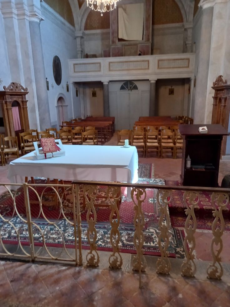 Interno di una chiesa con un tavolo apparecchiato e sedie in legno, caratterizzato da decorazioni architettoniche sobrie.