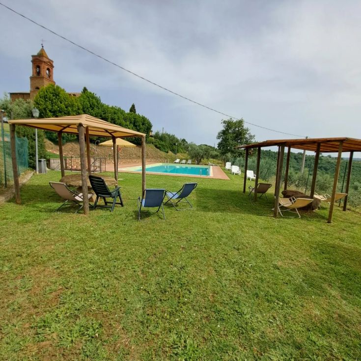 Un tranquillo giardino con piscina circondato da piante di ulivo e nei pressi di una storica chiesa.