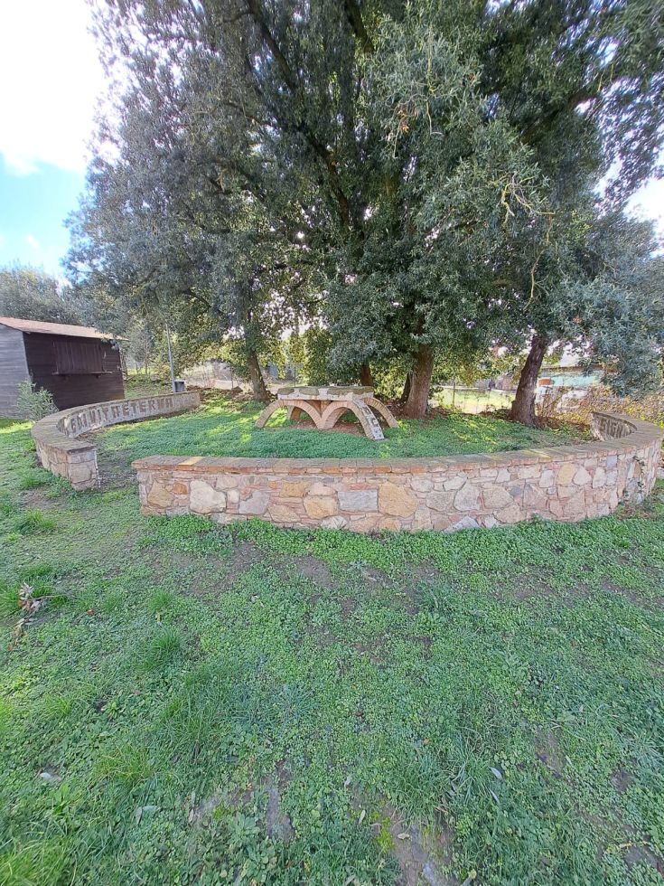 Un'area verde attrezzata con panchine in pietra e circondata da alberi, adatta per il relax e le passeggiate.