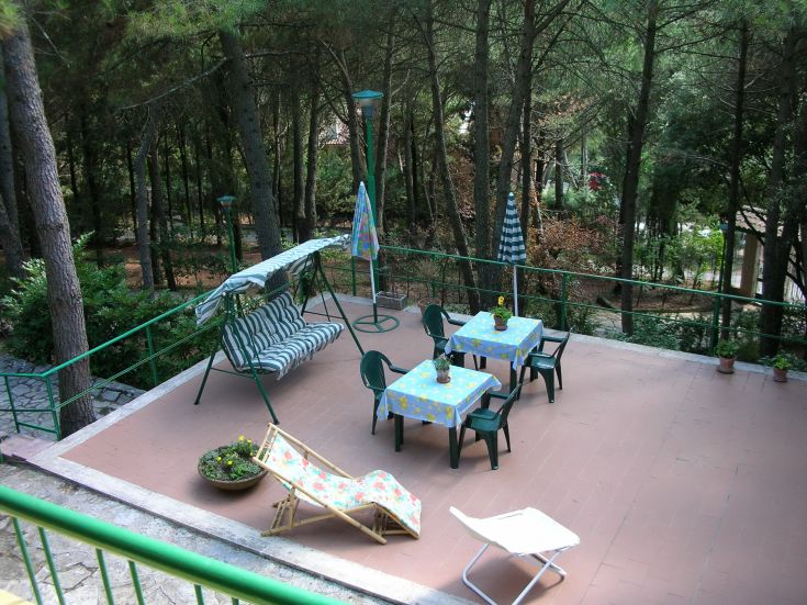 Outdoor relaxation area with tables, chairs, and umbrellas surrounded by trees and greenery.