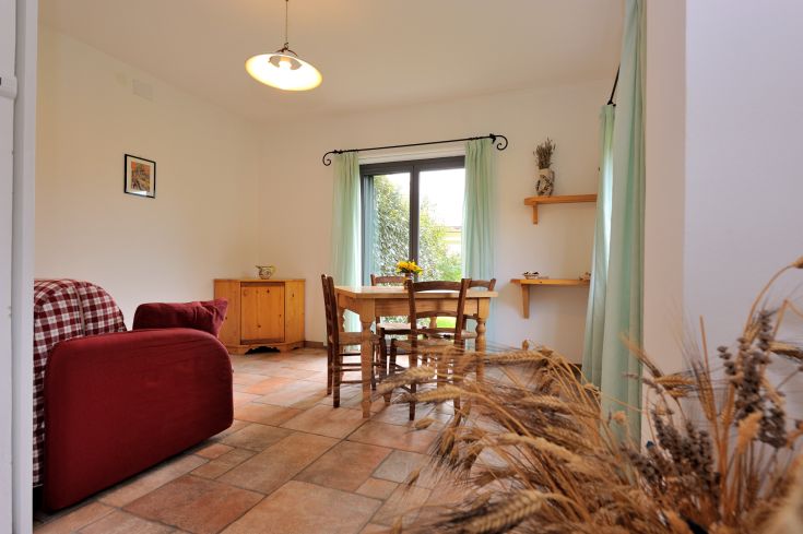 Ein gut beleuchtetes Wohnzimmer mit einem Tisch, Stühlen und einer kleinen Küchenzeile, bereichert durch natürliches Licht.