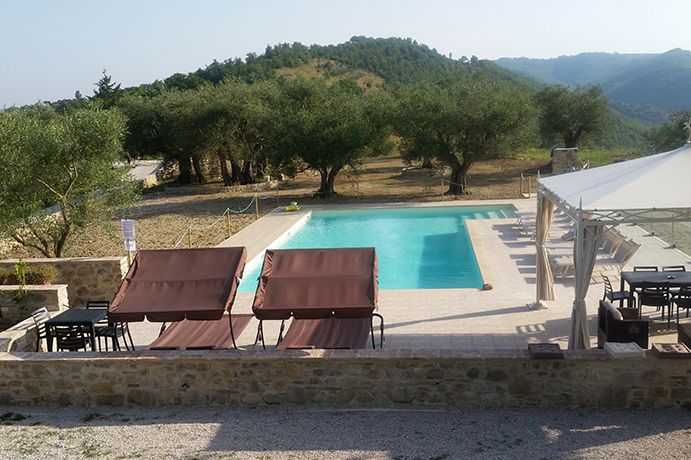 Une piscine entourée par la nature, avec des chaises longues disposées pour se détendre et une vue sur les collines environnantes.