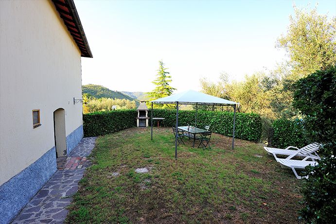 Ein entspannender Außenbereich mit einem Pavillon, einem Tisch und Stühlen, umgeben von Bäumen und Pflanzen.