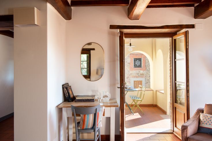 Un environnement intérieur confortable d'un agriturismo, avec une table et une chaise, donnant sur un patio extérieur lumineux.