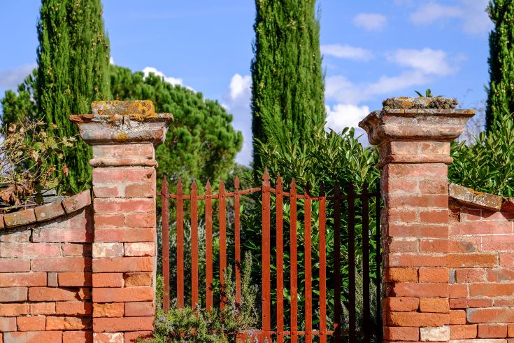 Un portail en briques rouges situé dans un environnement naturel avec des arbres et une végétation luxuriante.