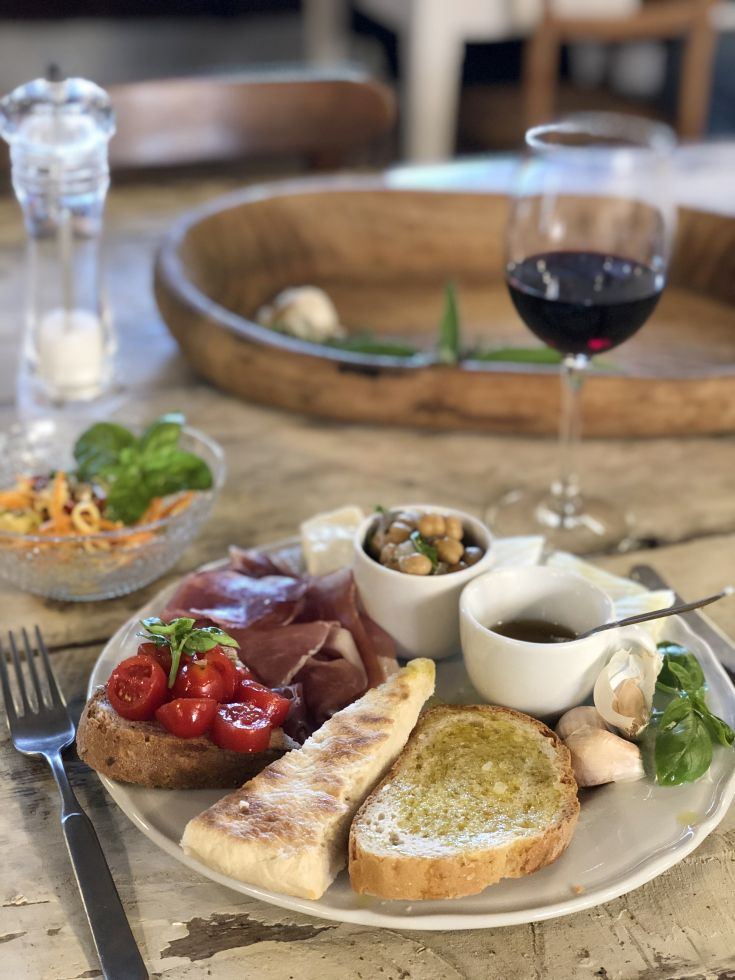 Un repas composé de bruschetta, de charcuterie variée et d'un verre de vin rouge, idéal pour un moment convivial.