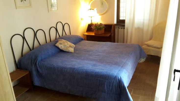 Bright matrimonial room with a blue bed, sober decor, and a view of a peaceful natural environment.