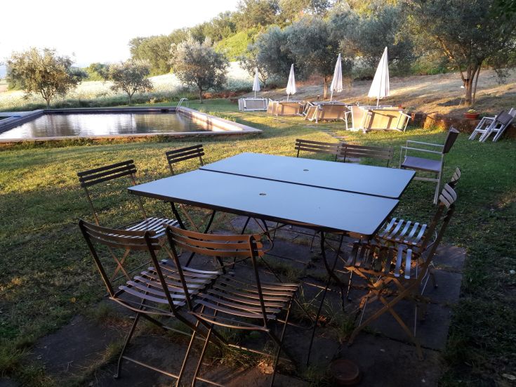 An outdoor table with chairs in a rural setting, next to a pool surrounded by nature.