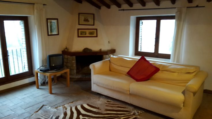 A living room in an Umbrian building, featuring exposed beams and a fireplace. Furnished in a simple, functional style.