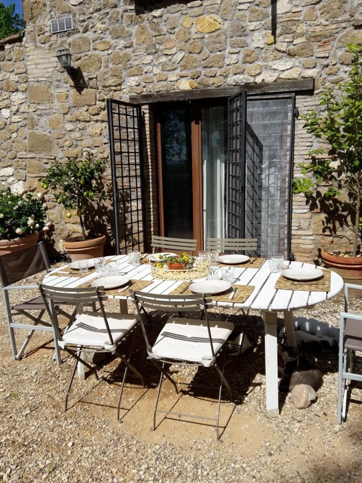 An outdoor table set for lunch, surrounded by plants with a stone building in the background.