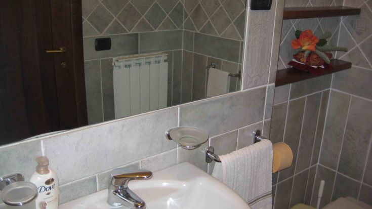Bagno semplice con piastrelle e accessori pratici, dotato di specchio e lavabo.